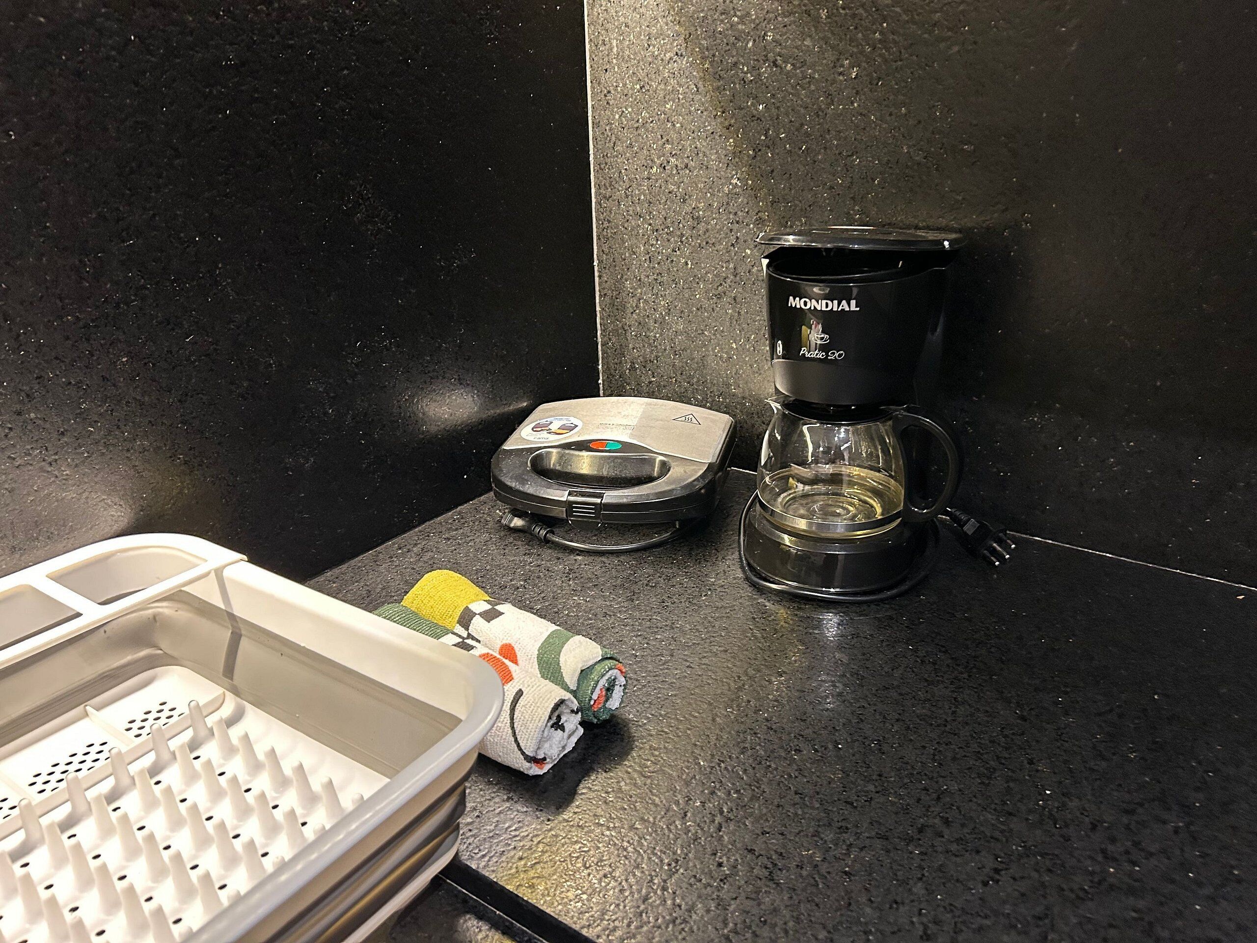 A kitchen counter with a coffee maker, a scale, and a container of sushi.