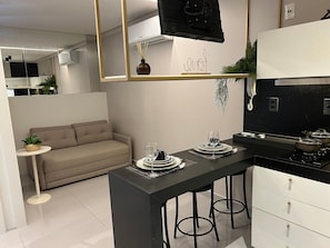 A modern kitchen with a central island, bar stools, a dining area with a sofa, and a small side table with a plant. - Bela Hospedagem - 607 One Way Tambau (Joao Pessoa)