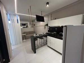 A modern kitchen with a central island, bar stools, a built-in oven, and a refrigerator. - Bela Hospedagem - 607 One Way Tambau (Joao Pessoa)