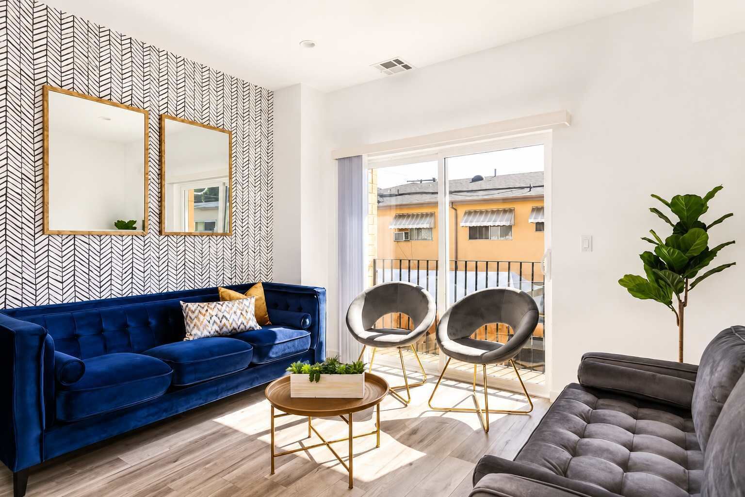 A living room with a blue sofa, two armchairs, a coffee table, and a large mirror on the wall.