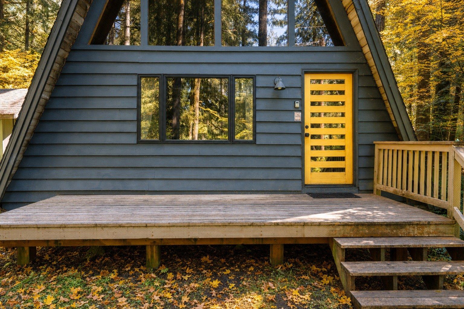 Une cabane avec une terrasse, une porte jaune et des fenêtres.