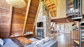 A cozy log cabin interior with a stone fireplace, wooden furniture, and a loft area. - Modern A-Frame - Hot Tub - Forest Escape (Rhododendron)