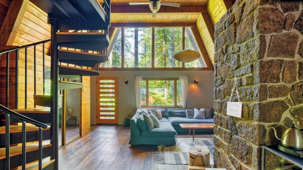 A spacious loft with a wooden staircase, a green sofa set, and a stone wall. - Modern A-Frame - Hot Tub - Forest Escape (Rhododendron)