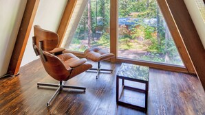 A room with a sloped ceiling, a large window, and a brown leather chair. - Modern A-Frame - Hot Tub - Forest Escape (Rhododendron)