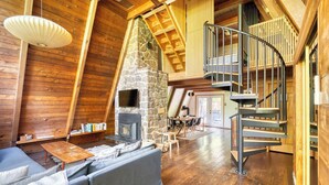 A cozy log cabin interior with a stone fireplace, wooden floors, a curved staircase, and a comfortable seating area. - Modern A-Frame - Hot Tub - Forest Escape (Rhododendron)