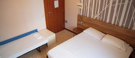 A room with a wooden bed, a single bed, a door with papers, a small bedside table, and a wall with a vertical pattern.