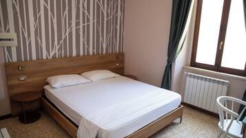 A bedroom with a wooden bed, a nightstand, a chair, a radiator, and a window with curtains.