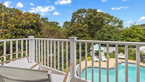 A poolside area with a white deck, lounge chairs, and a view of a swimming pool surrounded by trees. - Pool Loft Suite | Bay Access & Beach Passes (Annapolis)