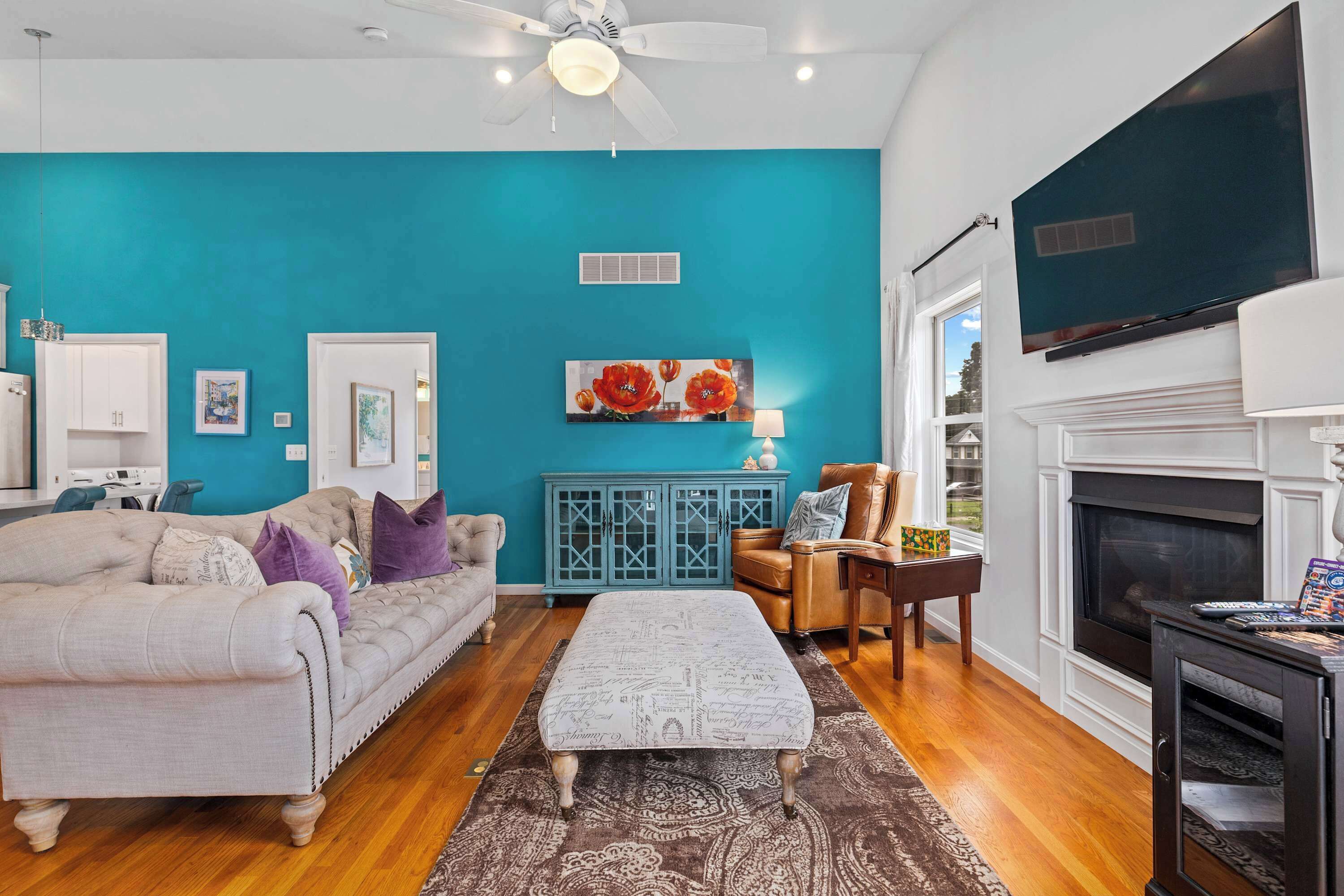 A living room with a teal wall, a white ceiling fan, a fireplace, and a television mounted above it.