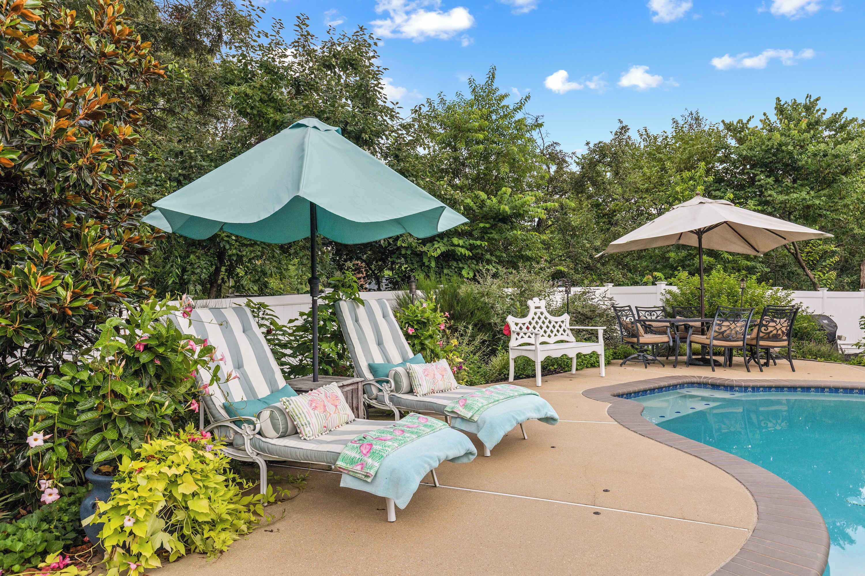 A poolside area with lounge chairs and umbrellas, surrounded by greenery.