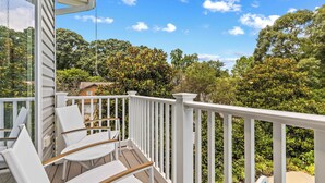 A deck with white railings and chairs, overlooking a lush garden and trees. - Pool Loft Suite | Bay Access & Beach Passes (Annapolis)