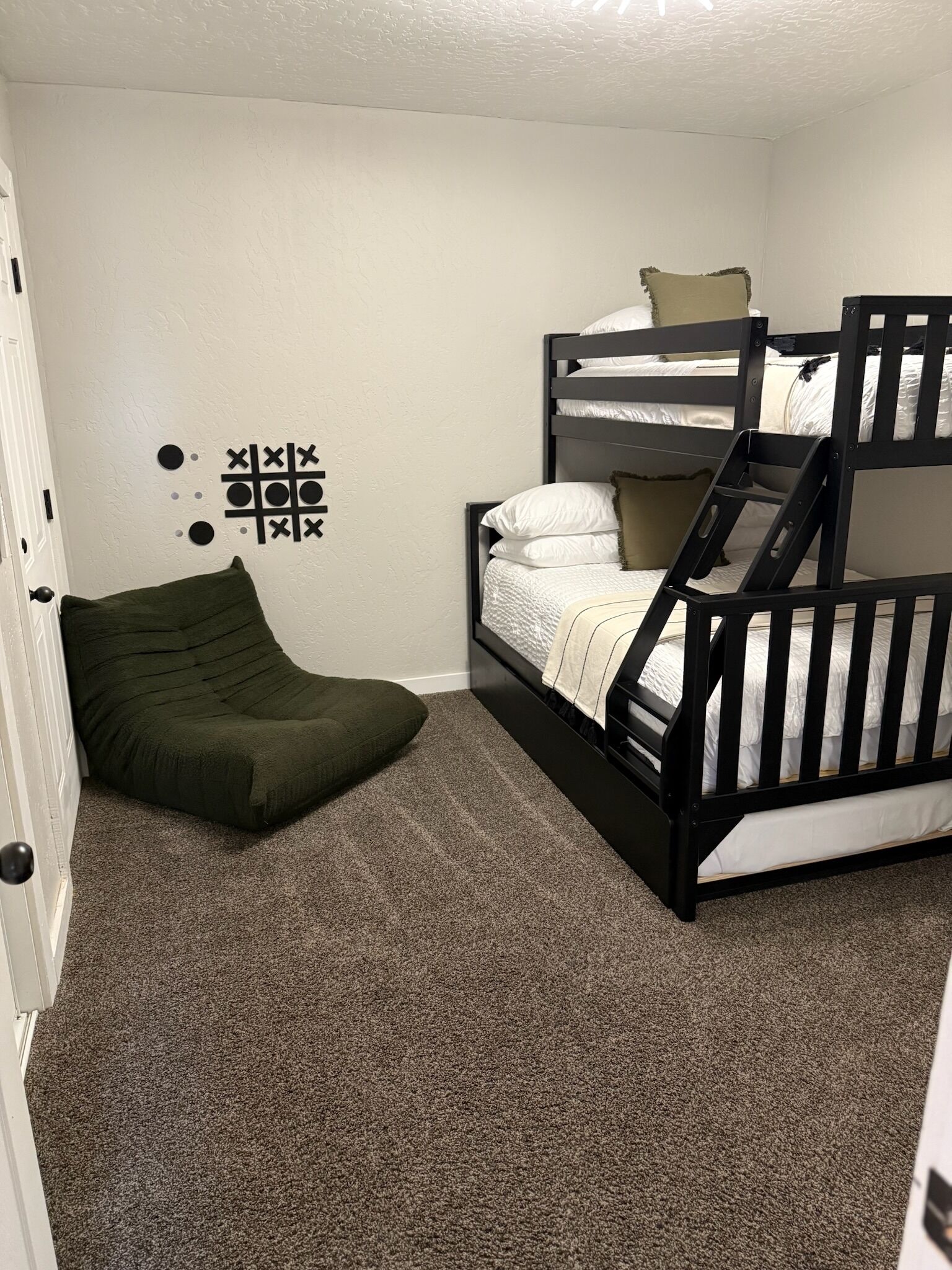 A bunk bed room with a green bean bag chair, a tic-tac-toe wall decoration, and a carpeted floor.