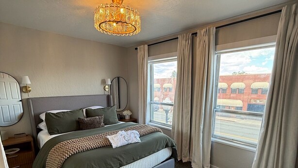 A hotel room with a bed, a nightstand, a lamp, and a window with curtains. - Historic Main Street Apartment A in Panguitch Utah (Panguitch)