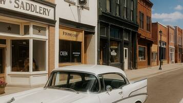 A classic white car parked on a street lined with historic buildings, including a cafe and a saddlery.