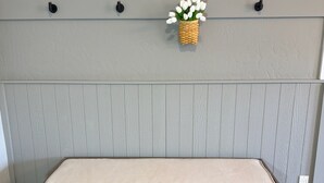 A bench with a cushioned seat and storage compartments, set against a textured wall with a basket of white flowers. - Historic Main Street Apartment A in Panguitch Utah (Panguitch)