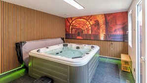 Een moderne badkamer met een vrijstaand bad, houten paneelwanden, een groot kunstwerk dat een industriële omgeving voorstelt, en een klein houten krukje.