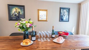 Een houten tafel met wijnflessen, glazen, een bloemenboeket en gebak.