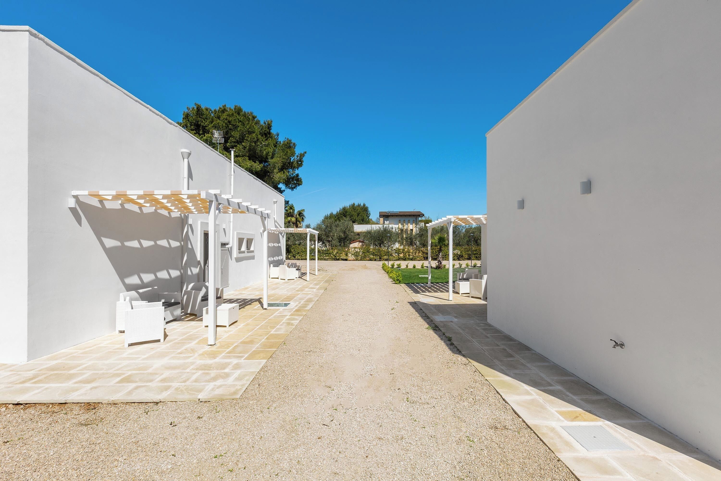Un chemin menant à un bâtiment doté d’une terrasse et d’une pergola.