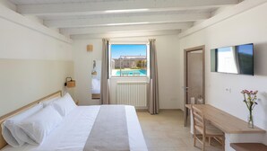 A bedroom with a bed, a wooden desk, a TV, and a window with a view of a pool. - B&B Giorò | Camera tripla (Galatone)