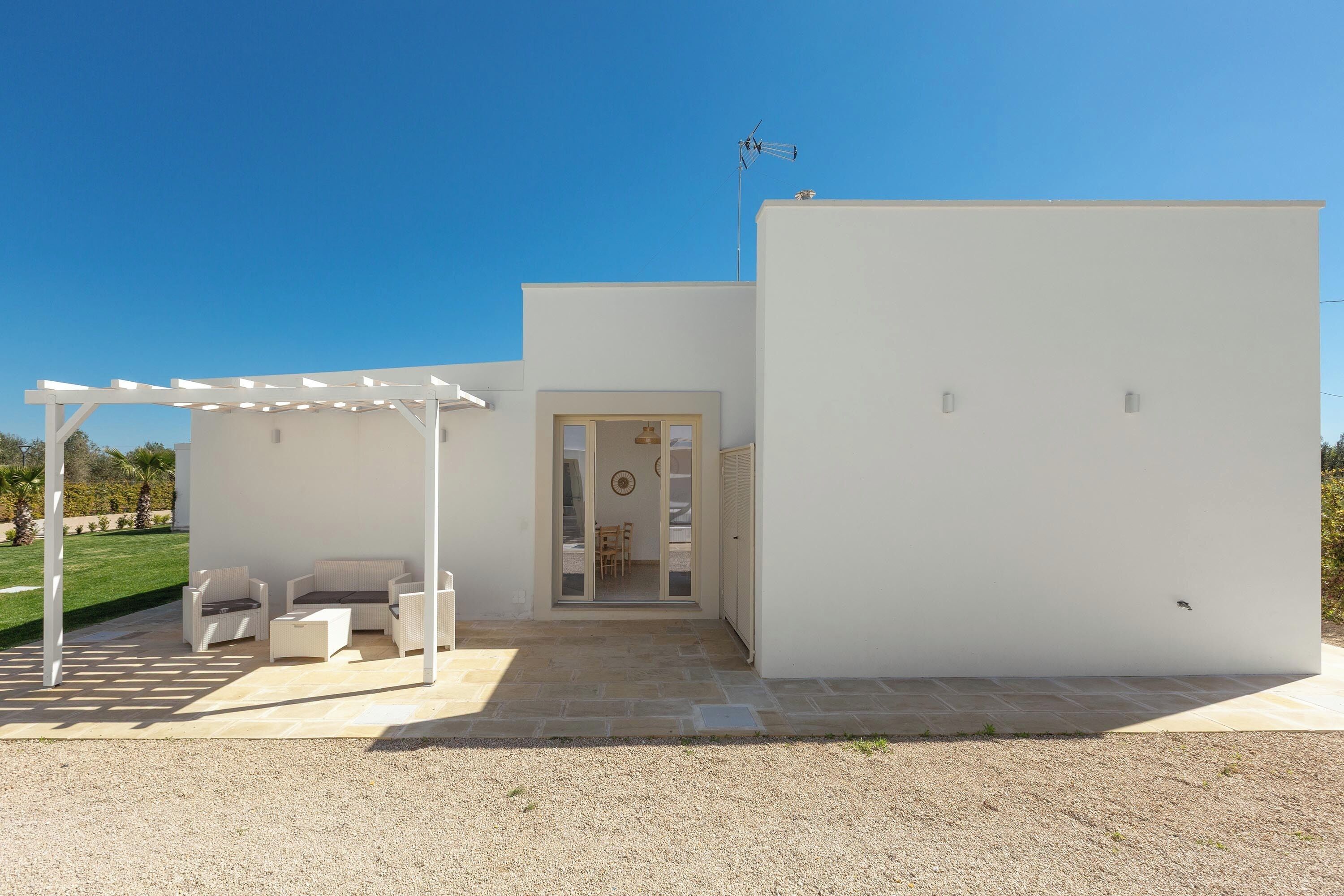 Un bâtiment moderne à l’extérieur blanc, doté d’un patio couvert avec des meubles d’extérieur, et surplombant un ciel dégagé.