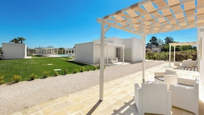 A covered outdoor seating area with white wicker furniture, a clear view of a pool, and a well-maintained lawn. - B&B Giorò | Camera tripla (Galatone)
