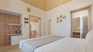 Un dormitorio con cama, una kitchenette pequeña, un espejo y un baño visible a través de una puerta abierta.