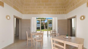 Un comedor amplio con mesas y sillas de madera, ventanas grandes con vistas a palmeras y un techo de piedra.