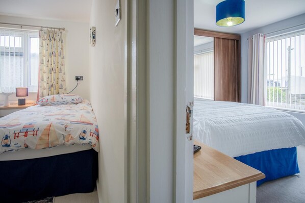 Ein Schlafzimmer mit zwei Betten, einem Fenster mit Vorhängen, einer Nachttischlampe und Blick ins Freie.