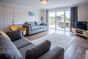 A modern living room with a grey sofa set, a yellow armchair, and a flat-screen TV.