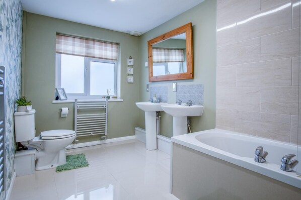 A bathroom with a toilet, two sinks, a bathtub, and a window with a curtain.