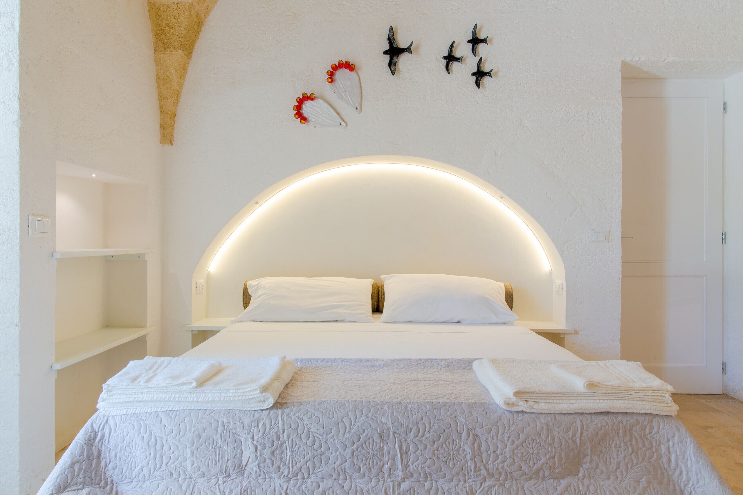 Ein modernes Hotelzimmer mit einem großen Bett, weißen Bettwäsche, einer gewölbten Decke und Wanddekorationen mit Vögeln und Blumen.