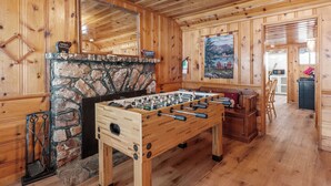 A wooden-floored room with a foosball table, stone fireplace, and a painting on the wall.