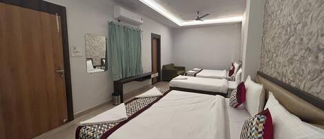 A hotel room with two beds, a desk, a chair, a ceiling fan, and a window with curtains.