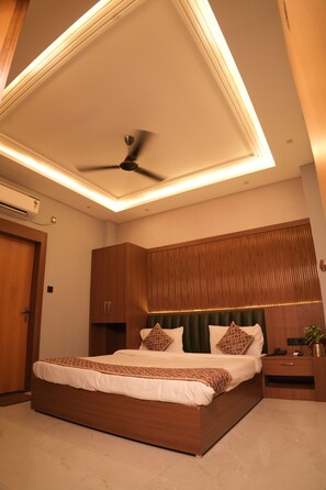 A bedroom with a bed, ceiling fan, bedside table, and a wall-mounted TV. - SANIDHYAM by HOTEL SAHU (Varanasi)