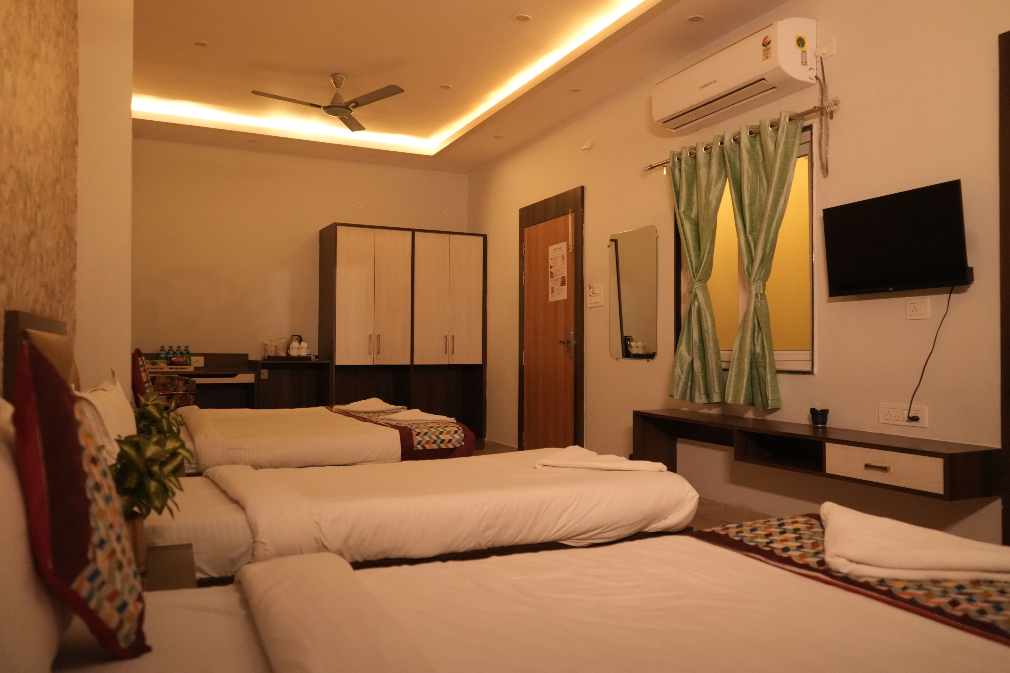 A hotel room with two beds, a ceiling fan, an air conditioning unit, a TV, and a small desk with a mirror.