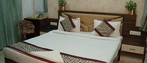 A hotel room with a large bed, a desk, a chair, a nightstand, a ceiling fan, and a wall-mounted mirror.