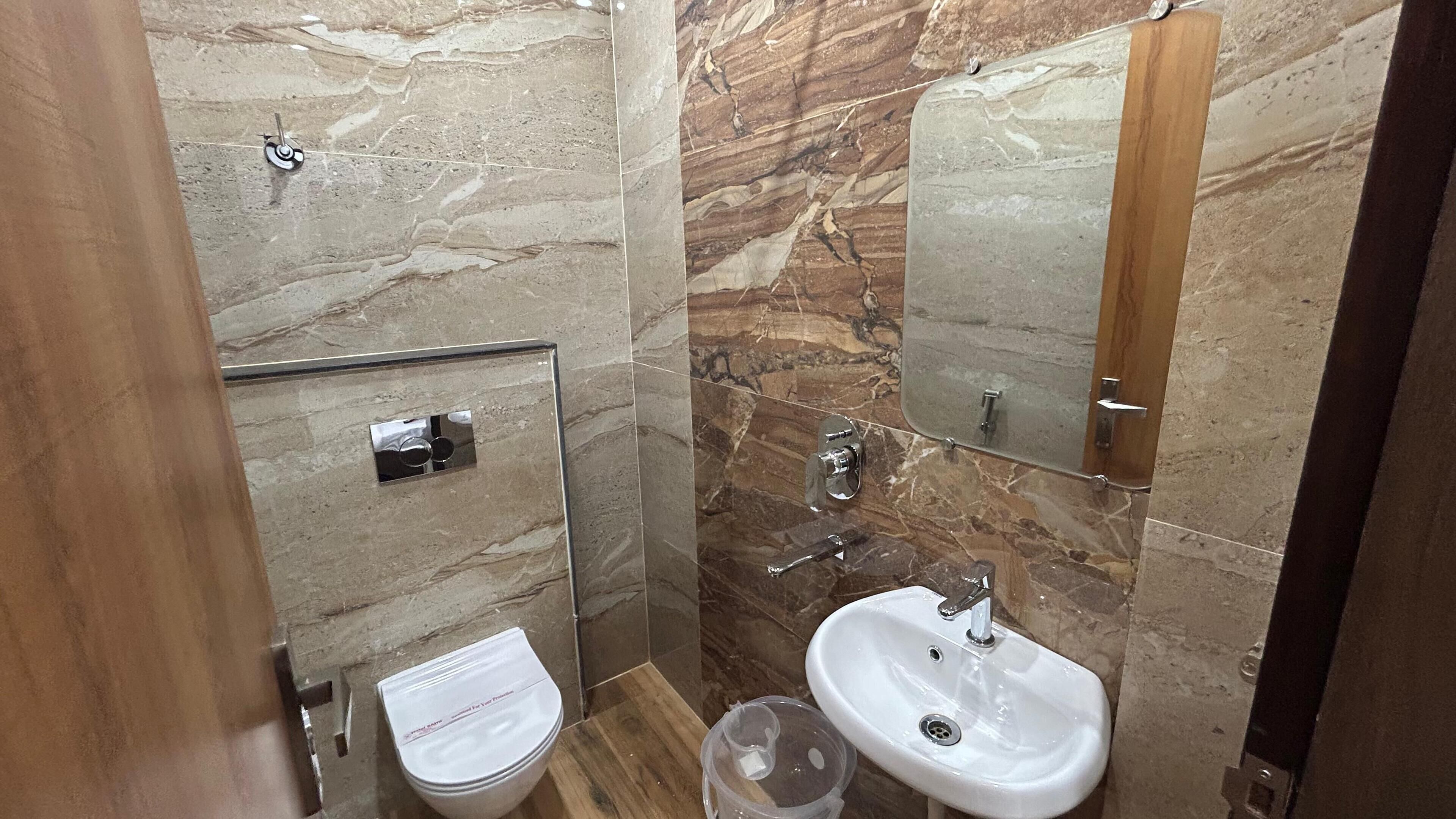 A bathroom with a marble wall, a toilet, a sink, and a shower.