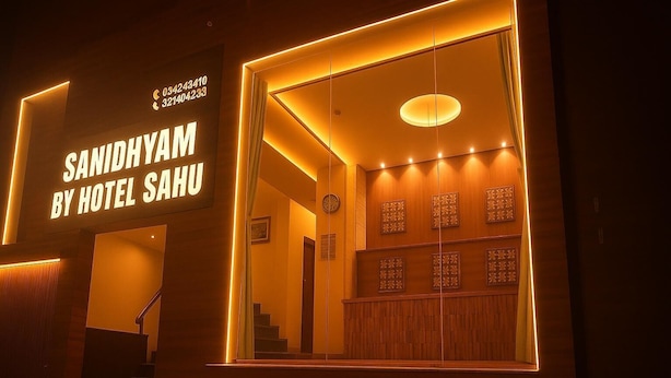The exterior of Sanidhyam by Hotel Sahu, featuring a modern design with a prominent entrance and a well-lit interior visible through the windows. - SANIDHYAM by HOTEL SAHU (Varanasi)