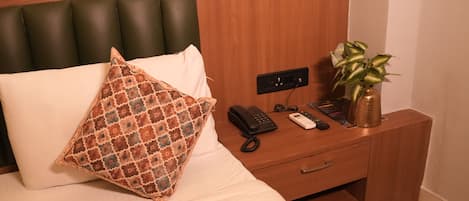 Ett hotellrum med en säng, ett nattduksbord med en telefon, en växt och en sänggavel i trä.