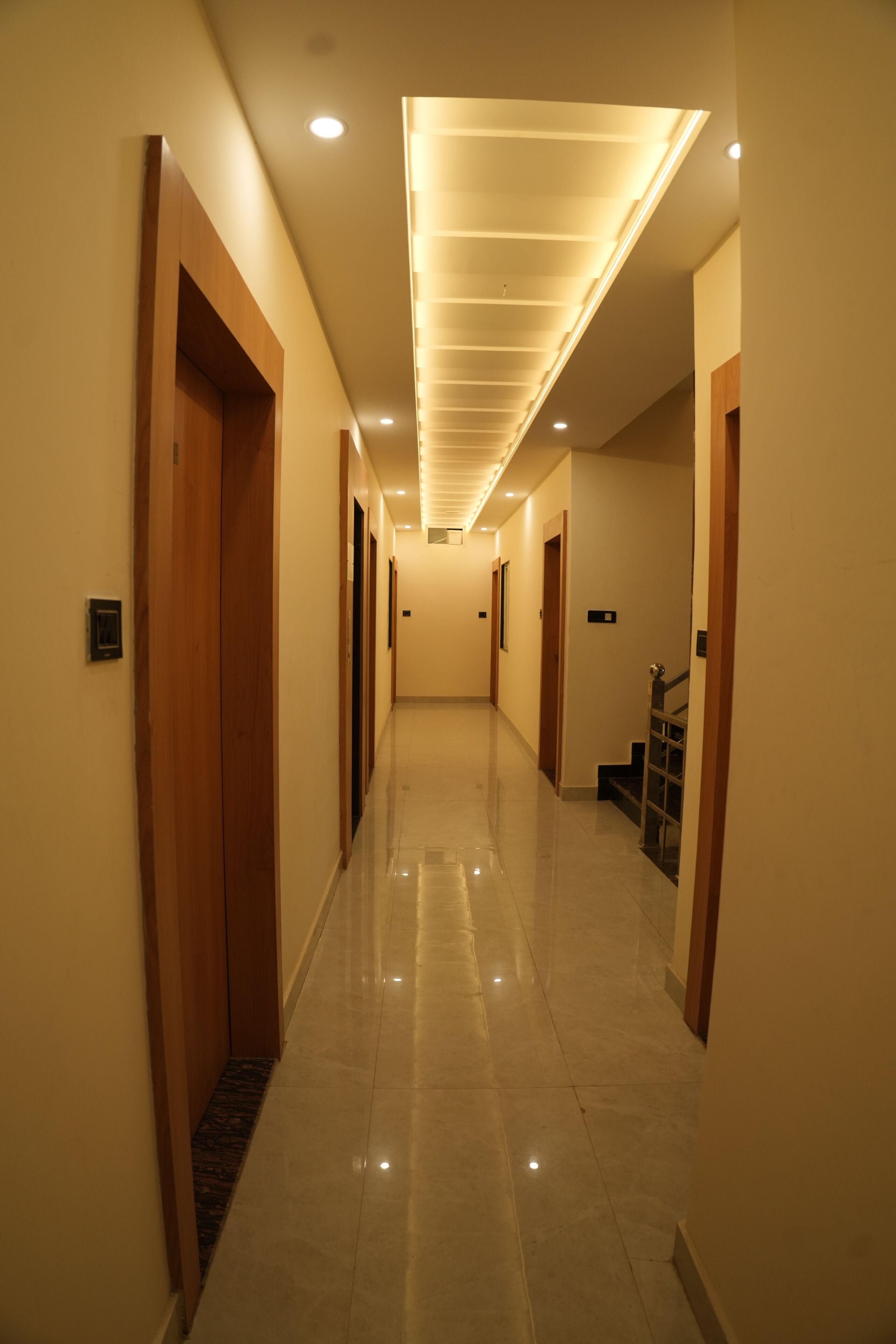 A hallway with wooden doors, a staircase, and recessed lighting.