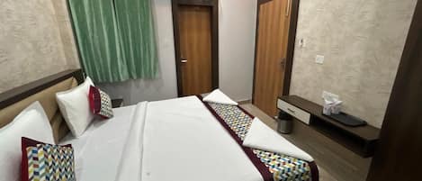Habitación de hotel con cama, una mesita de noche, un espejo, cortina verde y puerta de madera.