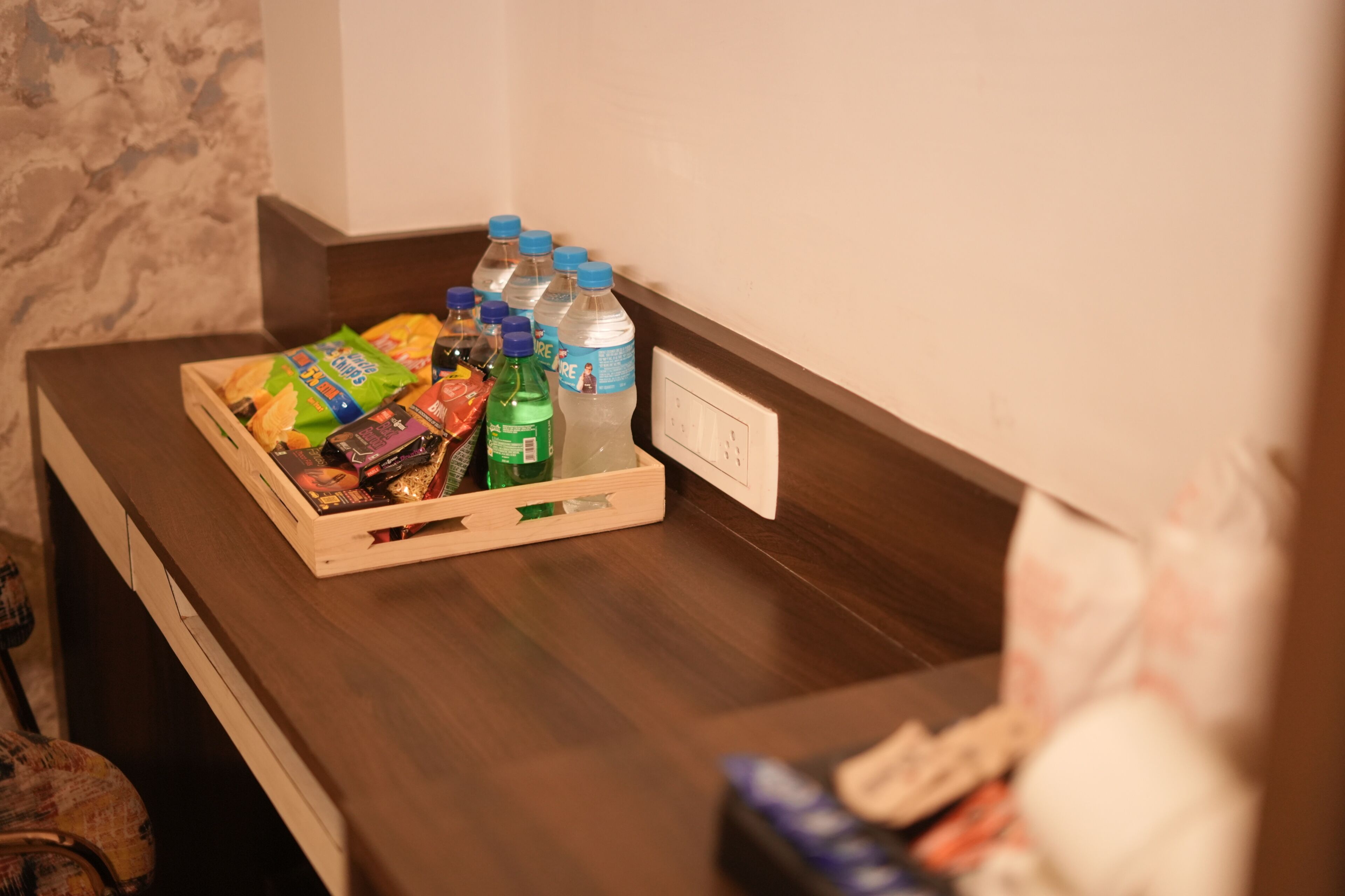 A wooden counter with a snack tray, bottled water, and a remote control.