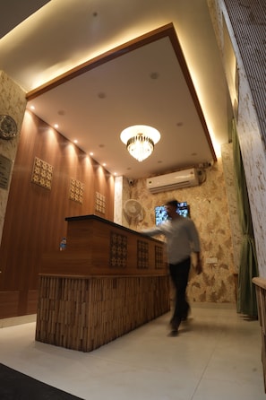 A reception area with a wooden reception desk, a chandelier, and an air conditioning unit on the wall.
