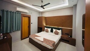 A modern bedroom with a large bed, wooden headboard, bedside tables, and a ceiling fan. - SANIDHYAM by HOTEL SAHU (Varanasi)