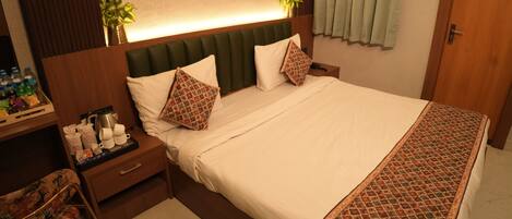 A neatly made bed with pillows, a bedside table with a lamp, a chair, and a small plant on the nightstand.