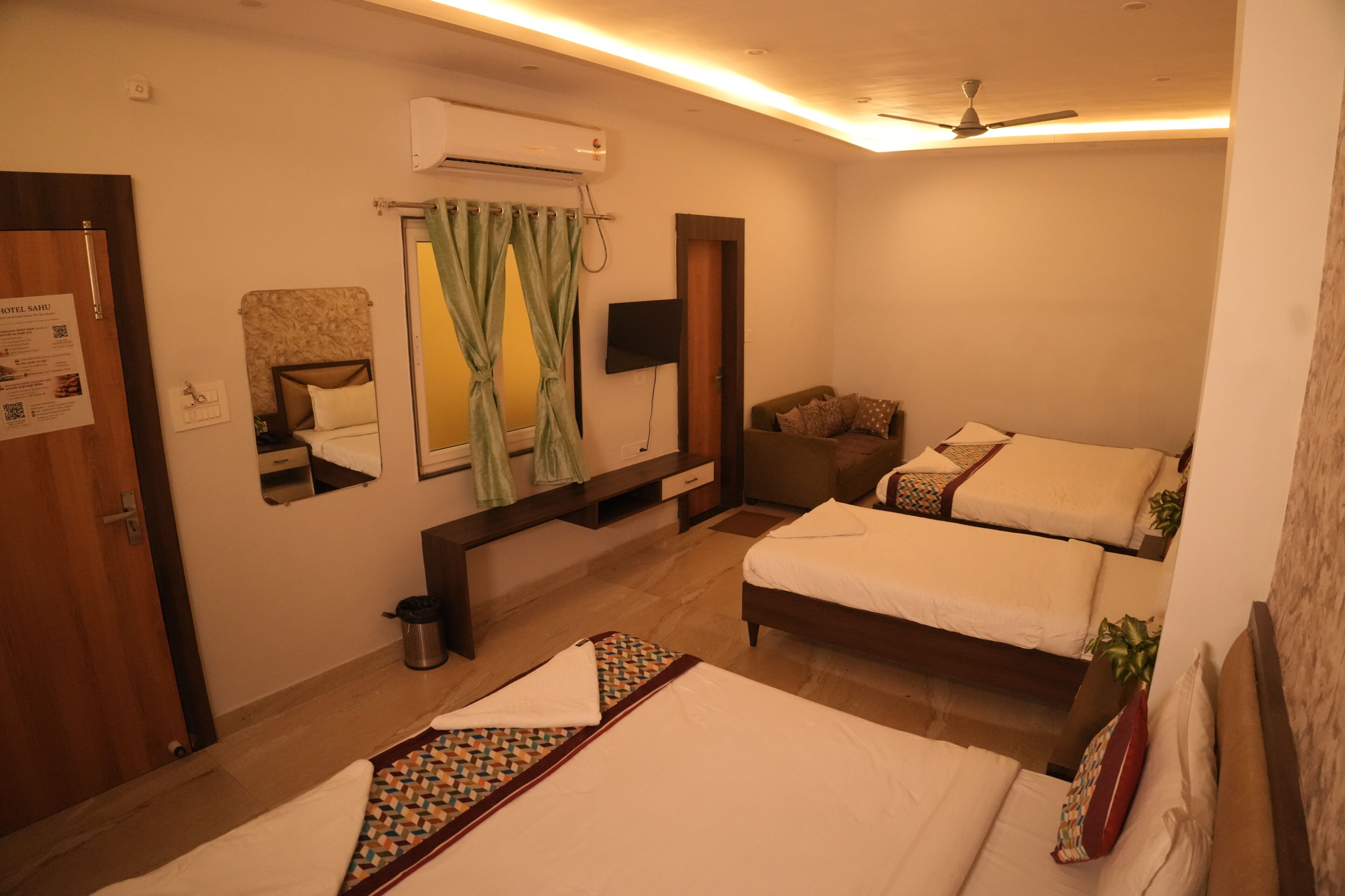 Habitación de hotel con dos camas, un escritorio, un espejo, aire acondicionado y ventilador de techo.