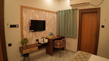 A hotel room with a wooden desk, a television, a small plant, a trash bin, and a door.