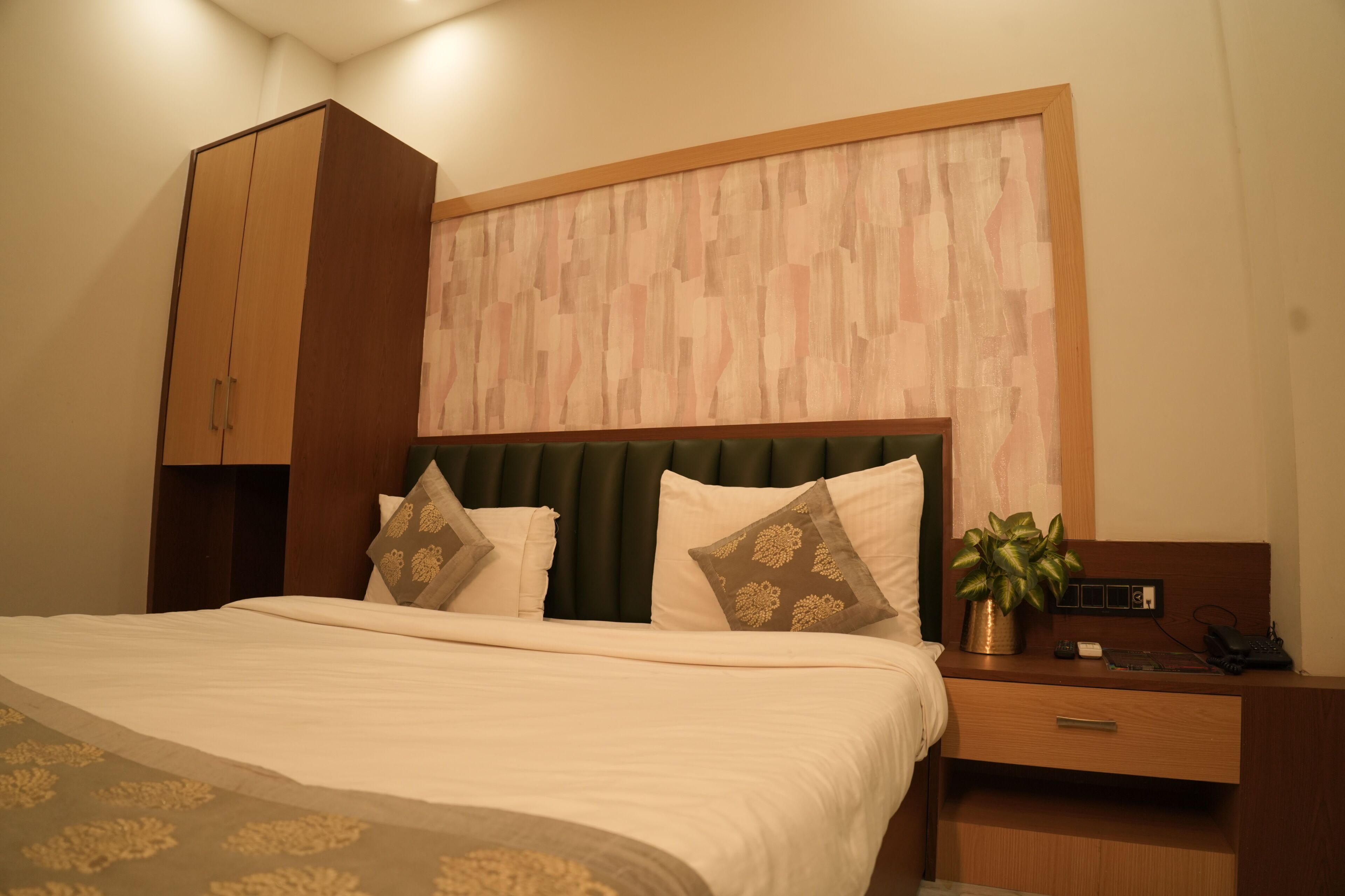 A hotel room with a bed, a nightstand, a drawer, a cabinet, and a wall-mounted plant.