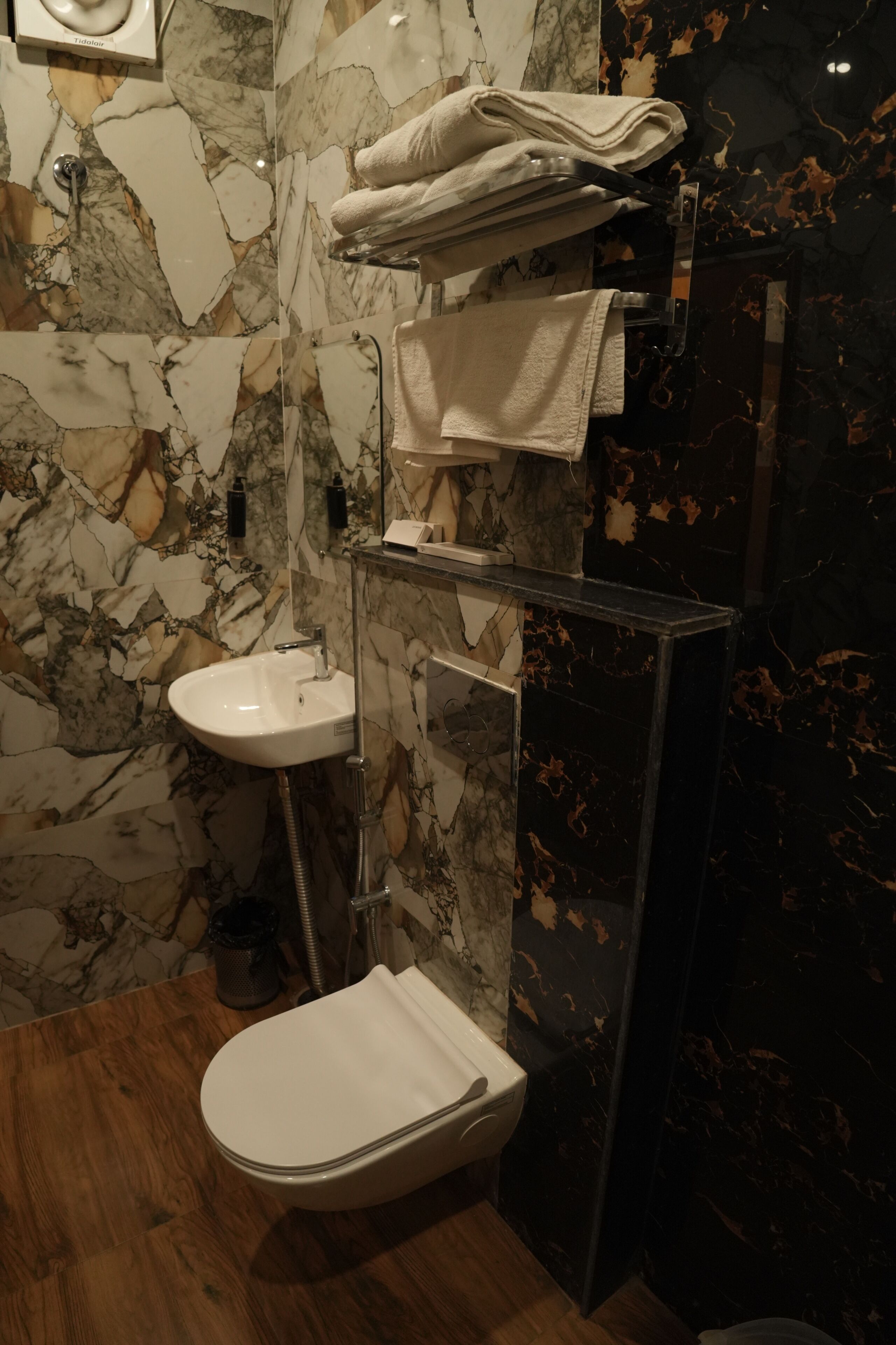 Een badkamer met een marmeren wand, een wit wastafeltje, een toilet en een handdoekhouder.
