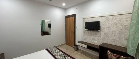 Un dormitorio con cama, escritorio, silla, televisor, ventilador de techo y una puerta.
